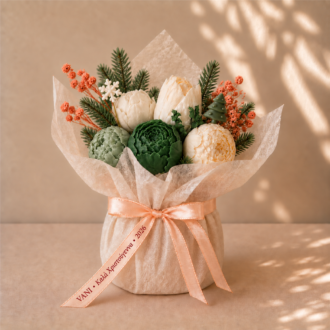 VANI Bouquet Ivoire de Noël — ιβουάρ και πράσινα λουλούδια από κερί με κέρινη νιφάδα και δεντράκι, σε ιβουάρ συσκευασία και σατέν κορδέλα με την ευχή Καλά Χριστούγεννα 2026.